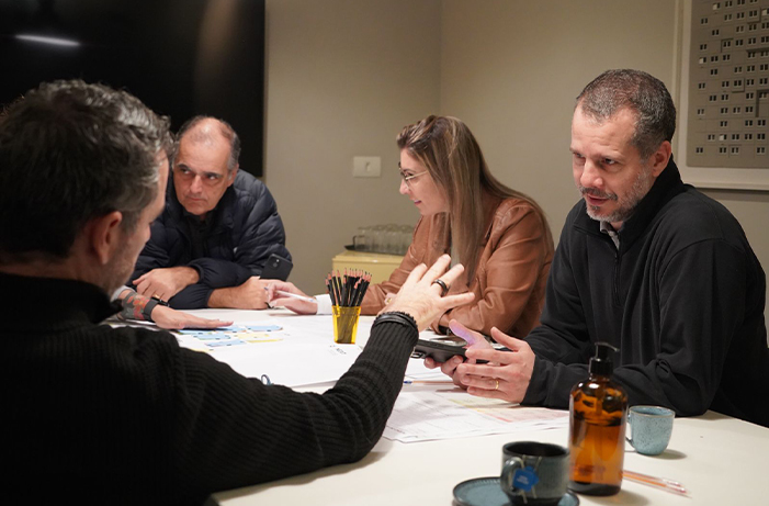 Grupo de pessoas discute materiais de trabalho em uma reunião colaborativa, representando a conexão entre áreas, troca de ideias e estruturação de programas de inovação.